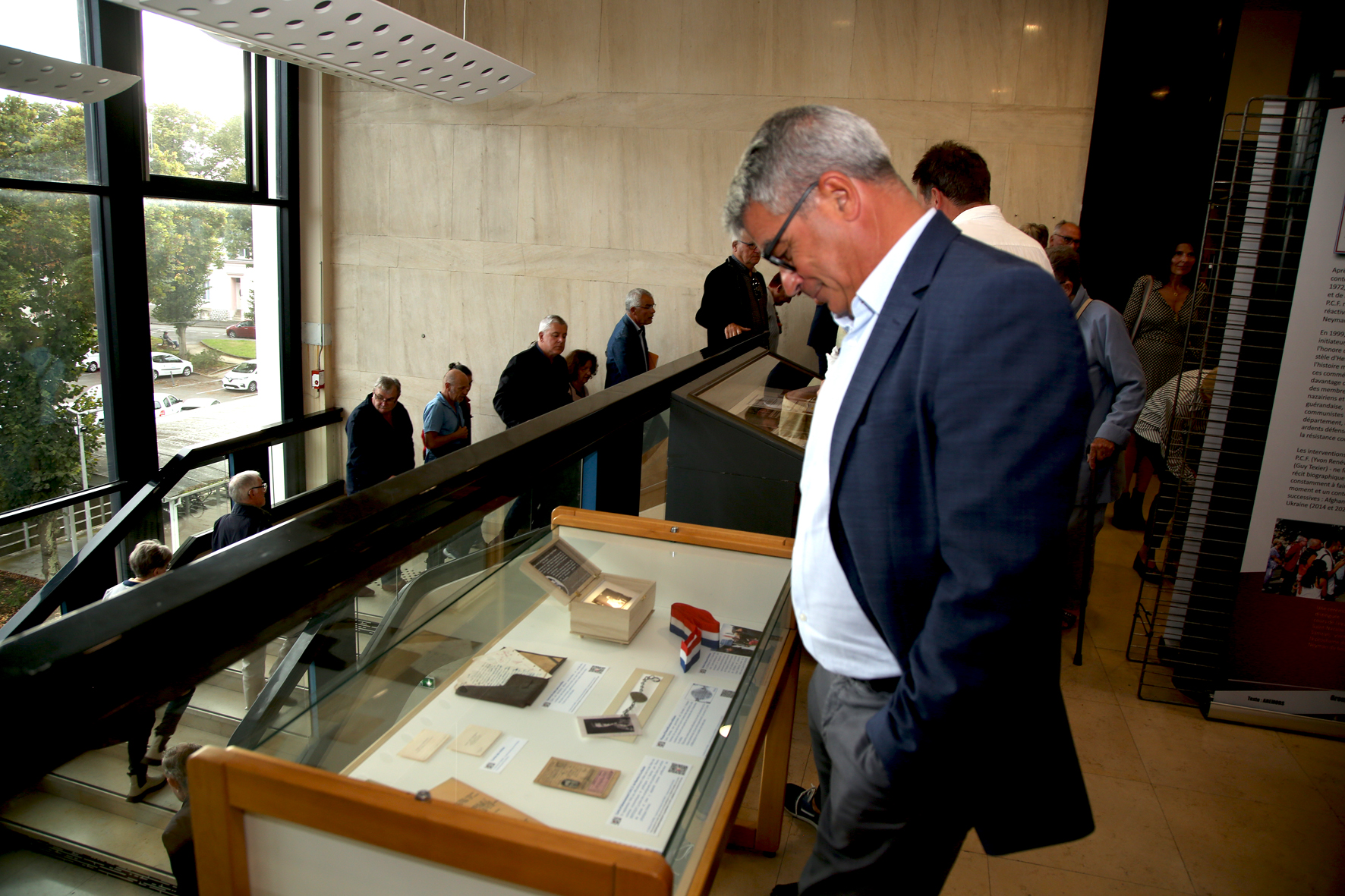 <p>David Samzun, maire de Saint-Nazaire, montre un fort intérêt sur la qualité de l'exposition et les objets de Jean exposés en vitrine.</p>© Photo [<acronym title="Patrice Morel">P.M.</acronym>->33] / Collectif <acronym title="Jean de Neyman">J.d.N.</acronym>, 20240905-9784.